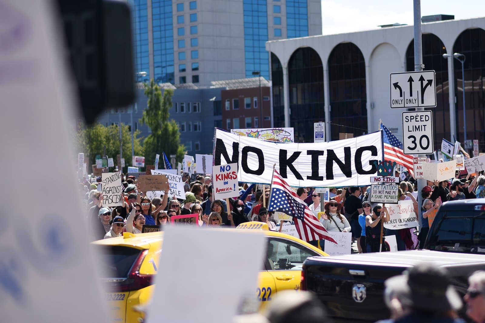 Protesters carry a large banner reading No King during a demonstration held on a sunny day in downtown Anchorage, Alaska.