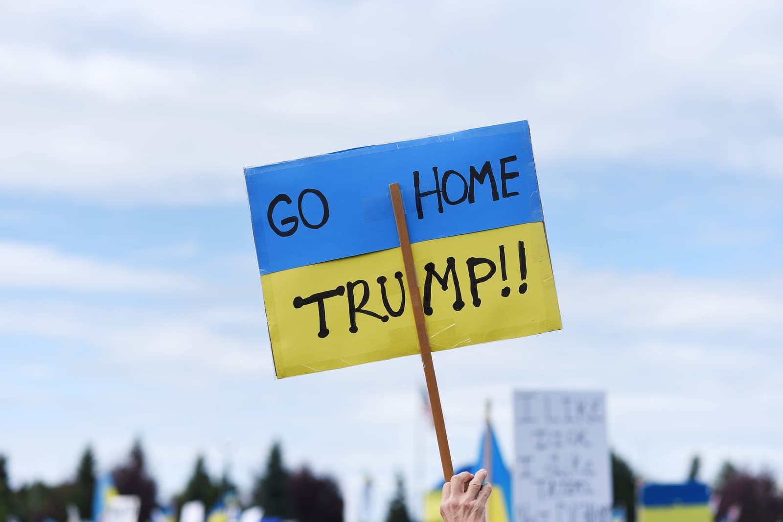 A hand-held sign painted in the colors of the Ukrainian flag reading Go Home Trump at a protest in downtown Anchorage, Alaska.