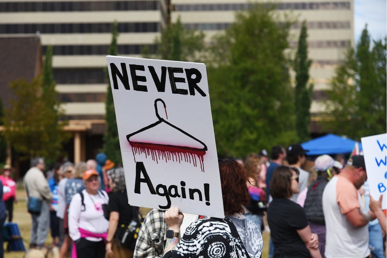 A protester holds a sign featuring a wire coat hanger and the words Never Again during a Planned Parenthood rally in downtown Anchorage, Alaska.