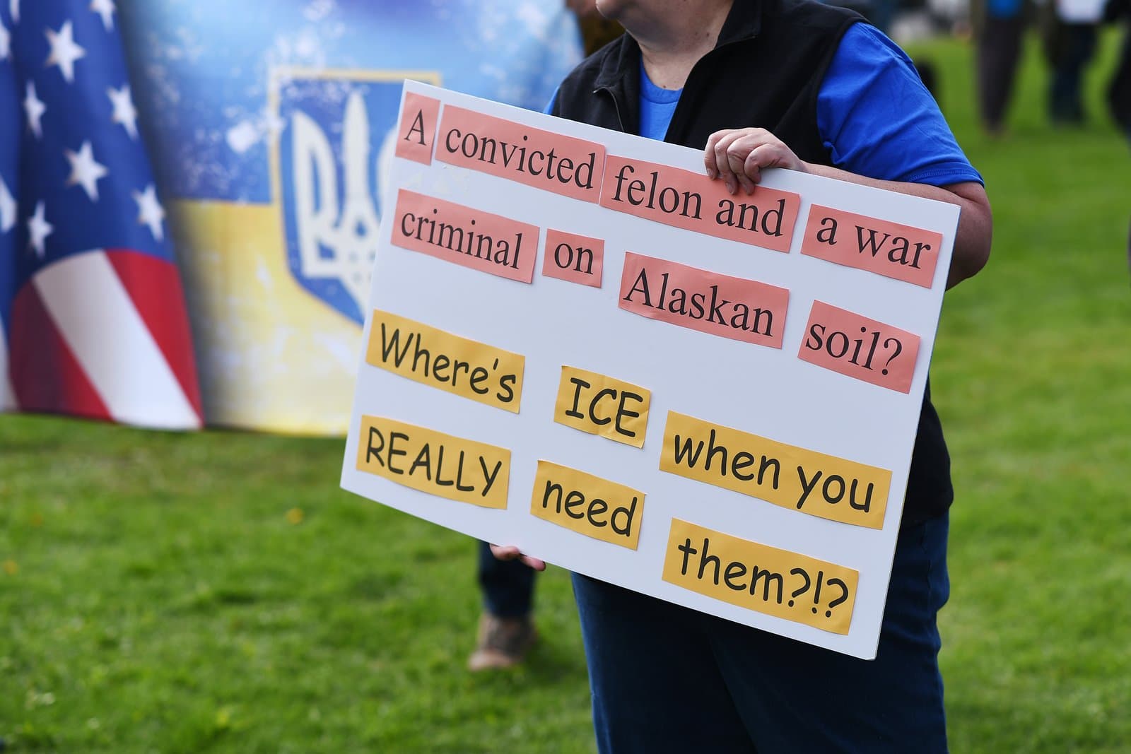 A protester holds a sign questioning the presence of a convicted felon and war criminal on Alaskan soil during a downtown Anchorage rally.