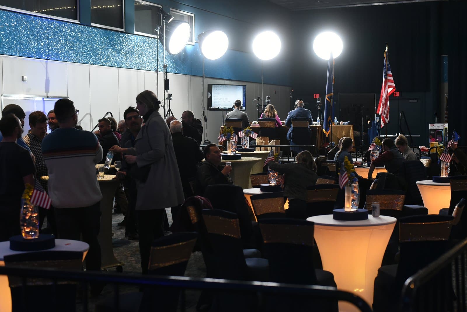Attendees gather at Election Central in November 2024, featuring illuminated tables, American flags, and professional lighting equipment in a large event space.