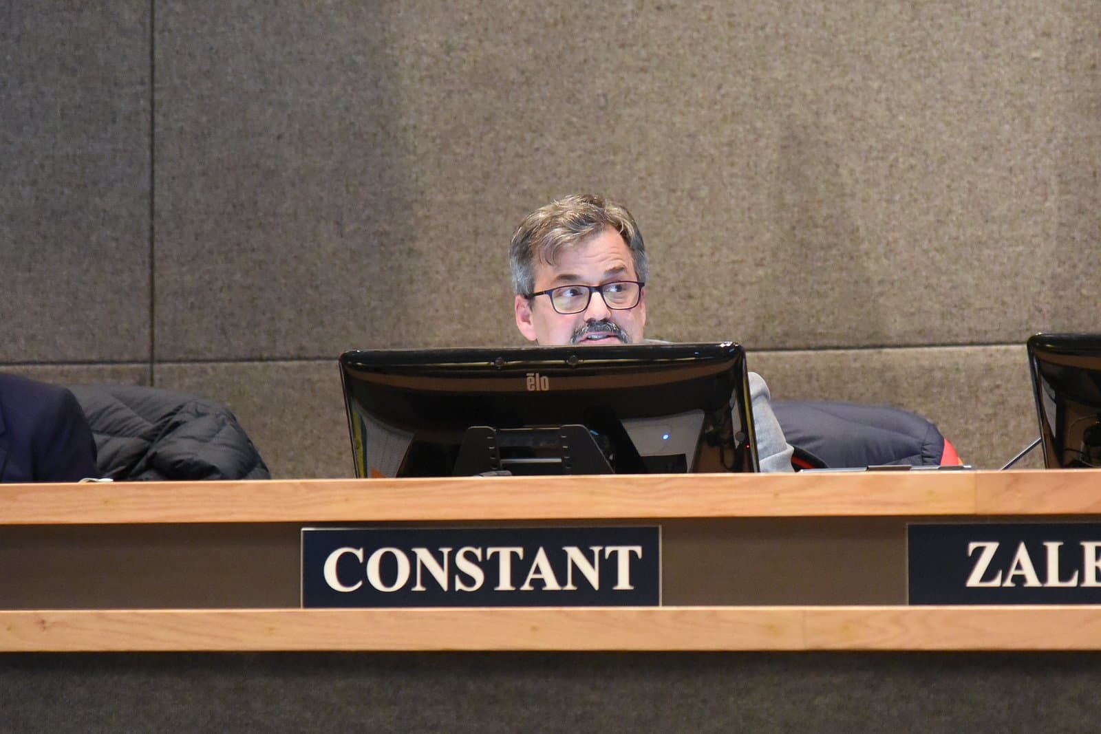 Assembly Member Christopher Constant sits at a desk with a nameplate during a public meeting in Anchorage, Alaska.