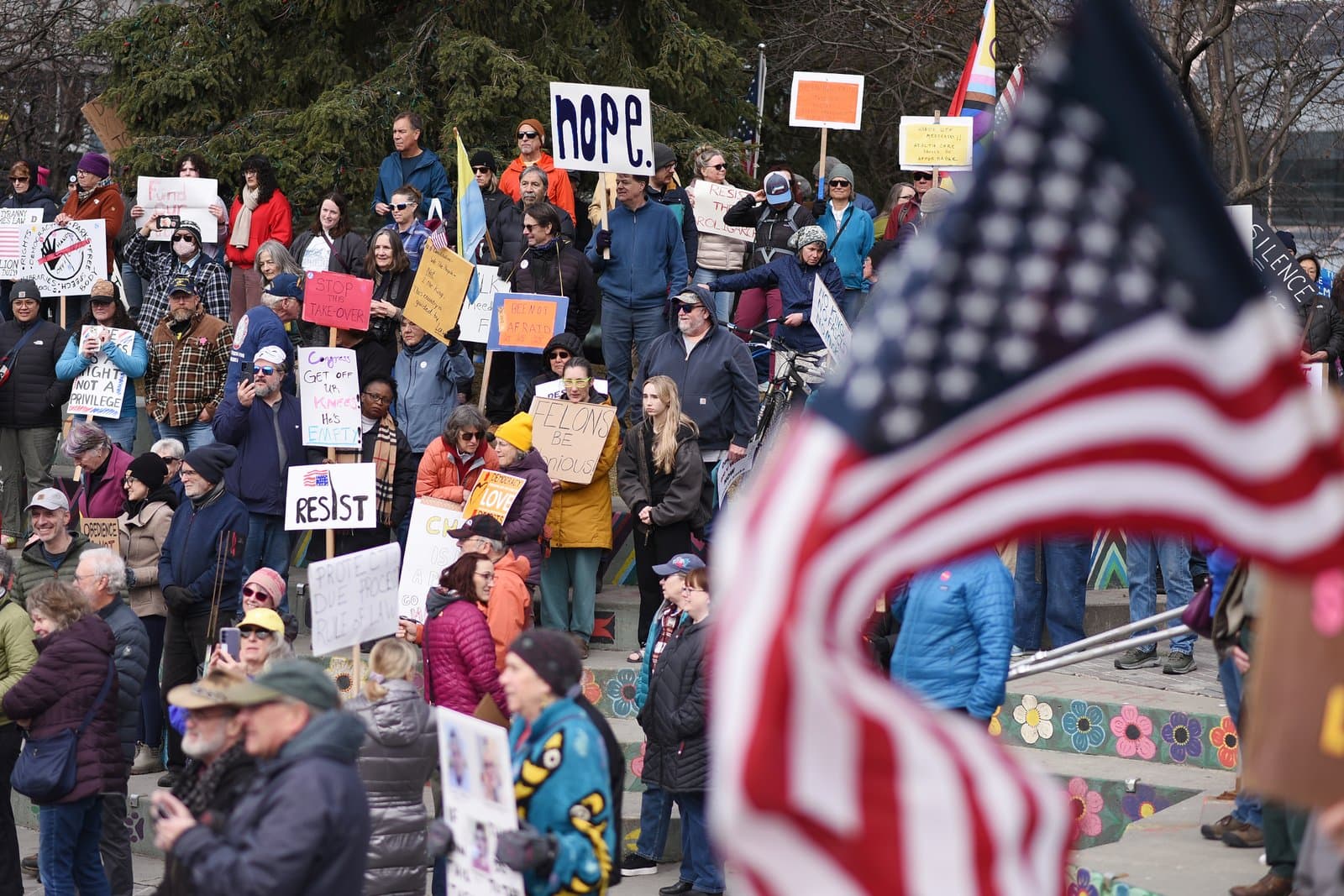 A diverse group of protesters holds signs and gathers on steps during a public demonstration in Anchorage, Alaska, on April 19, 2025.
