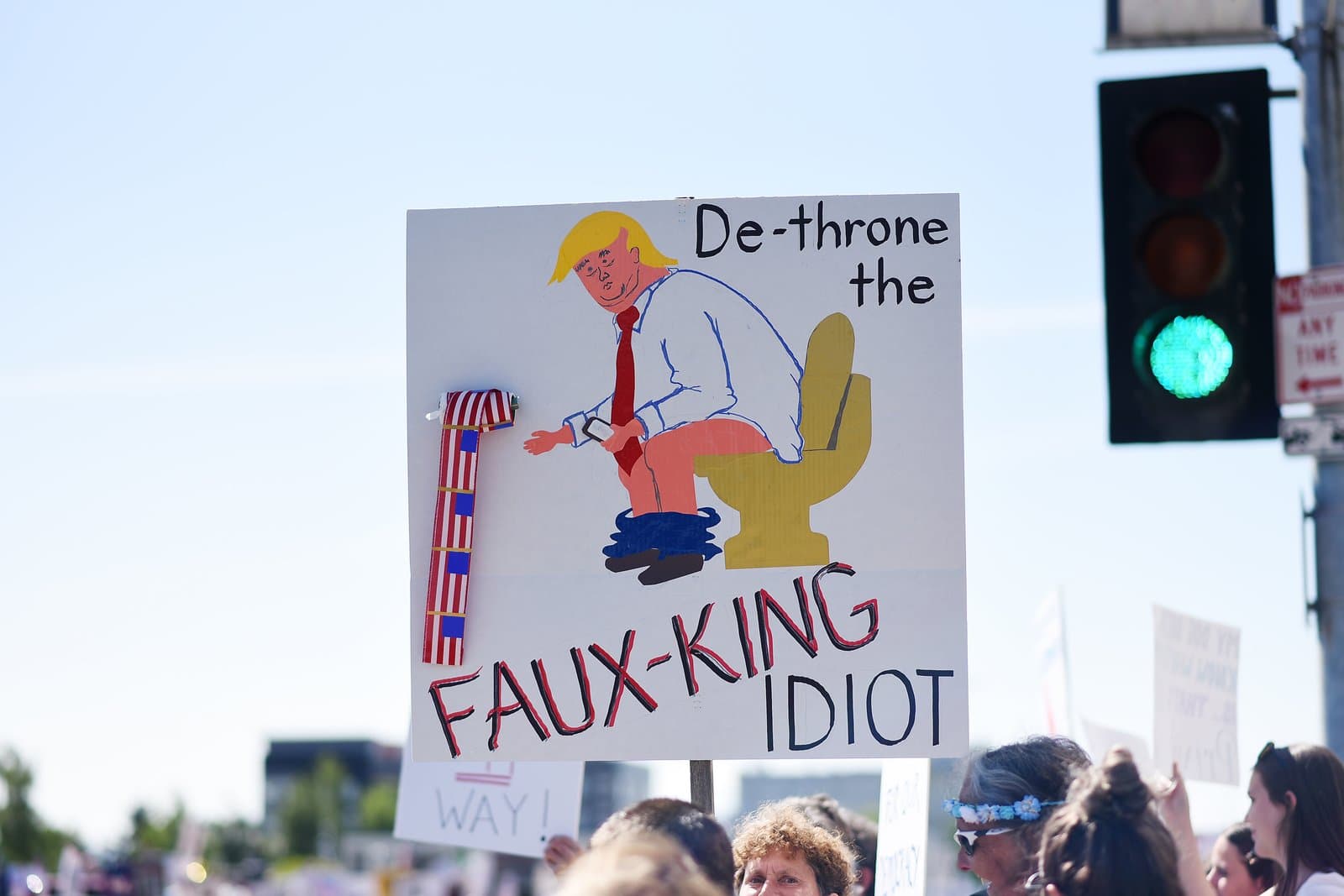 A protest sign featuring a cartoon illustration of Donald Trump on a toilet is held up during a demonstration in Anchorage, Alaska.