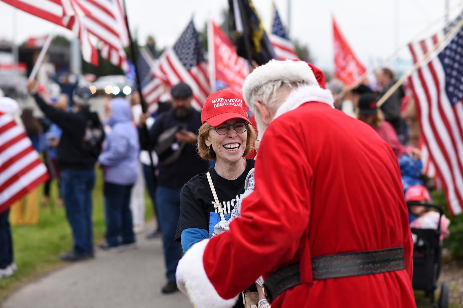 A woman wearing a red Make America Great Again hat smiles while interacting with a person dressed as Santa Claus at a rally.