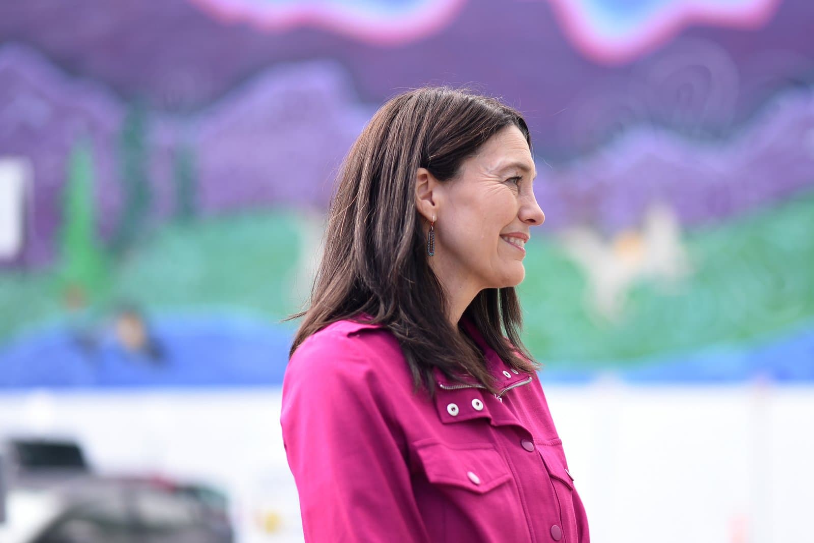 Suzanne LaFrance smiles while standing in front of a colorful mural during a campaign endorsement event in Anchorage, Alaska.