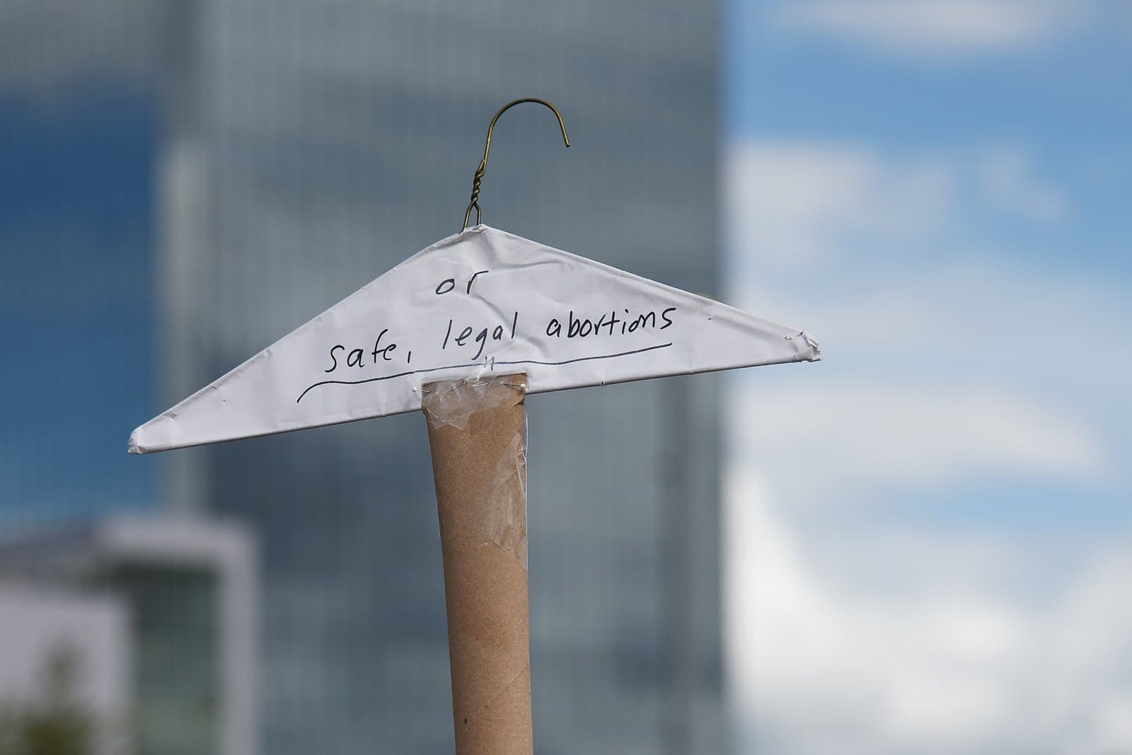 A handmade protest sign featuring a wire hanger and the text or safe, legal abortions is held during a rally in downtown Anchorage, Alaska.