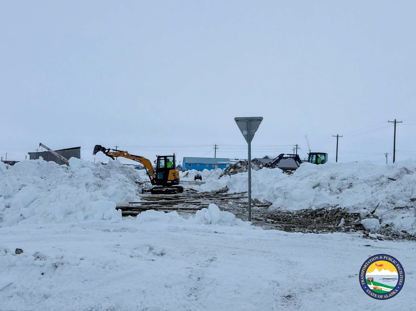 Two excavators clear heavy snow piles near a building in the community of Kipnuk, Alaska, during an April cleanup operation.