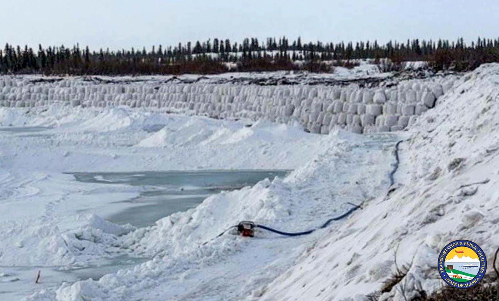A long wall of white sandbags protects a snowy, icy landscape in Noatak, Alaska, during spring flood mitigation efforts.