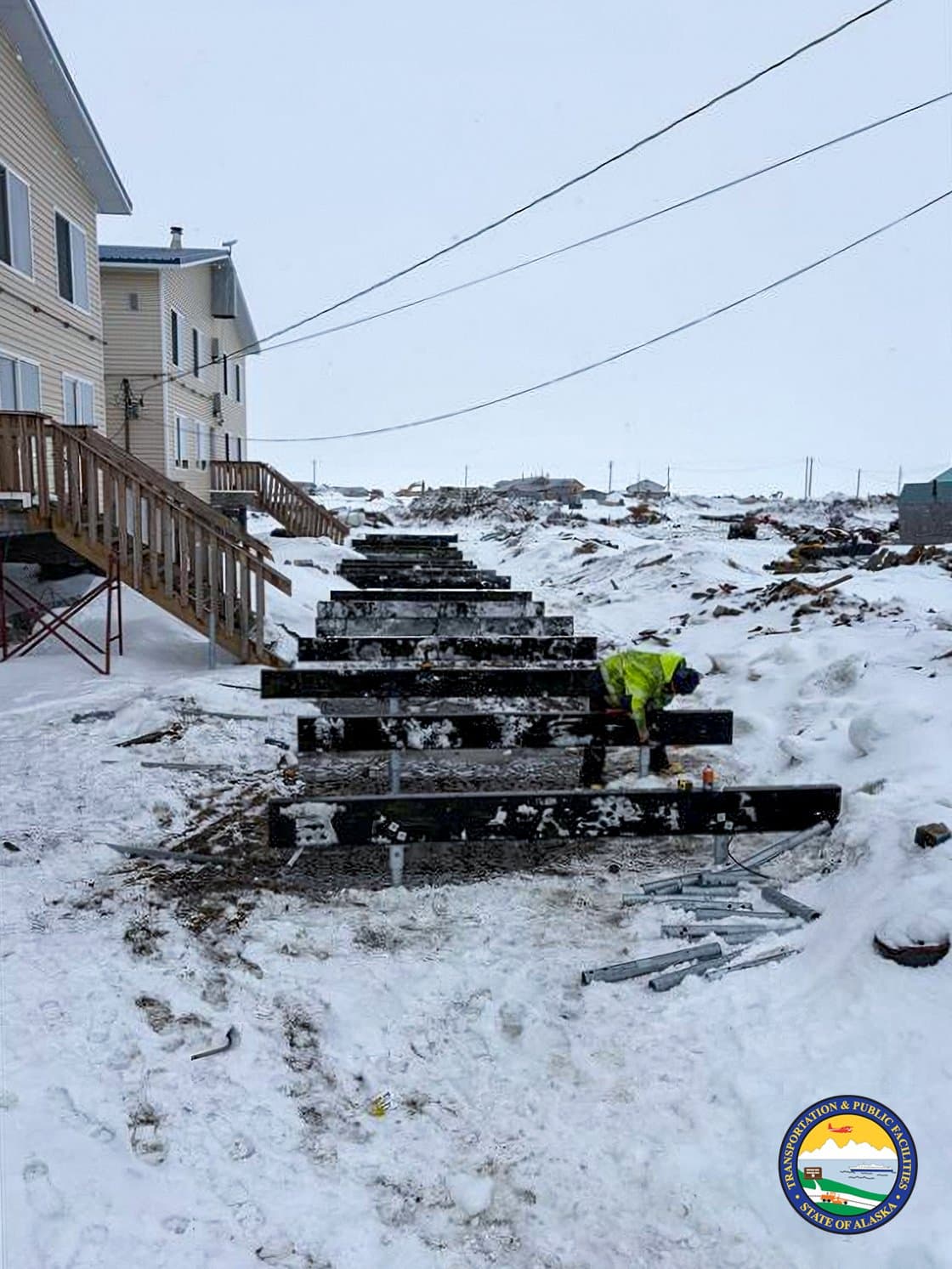 A construction worker in a high-visibility jacket installs foundation beams in the snow-covered village of Kipnuk, Alaska, during April.
