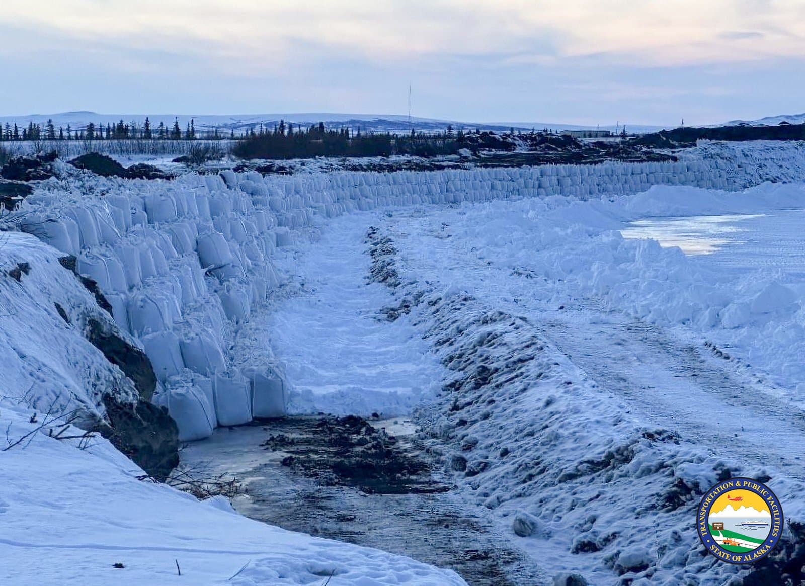 A long wall of white sandbags protects the snowy landscape of Noatak, Alaska, during the spring thaw in April 2026.
