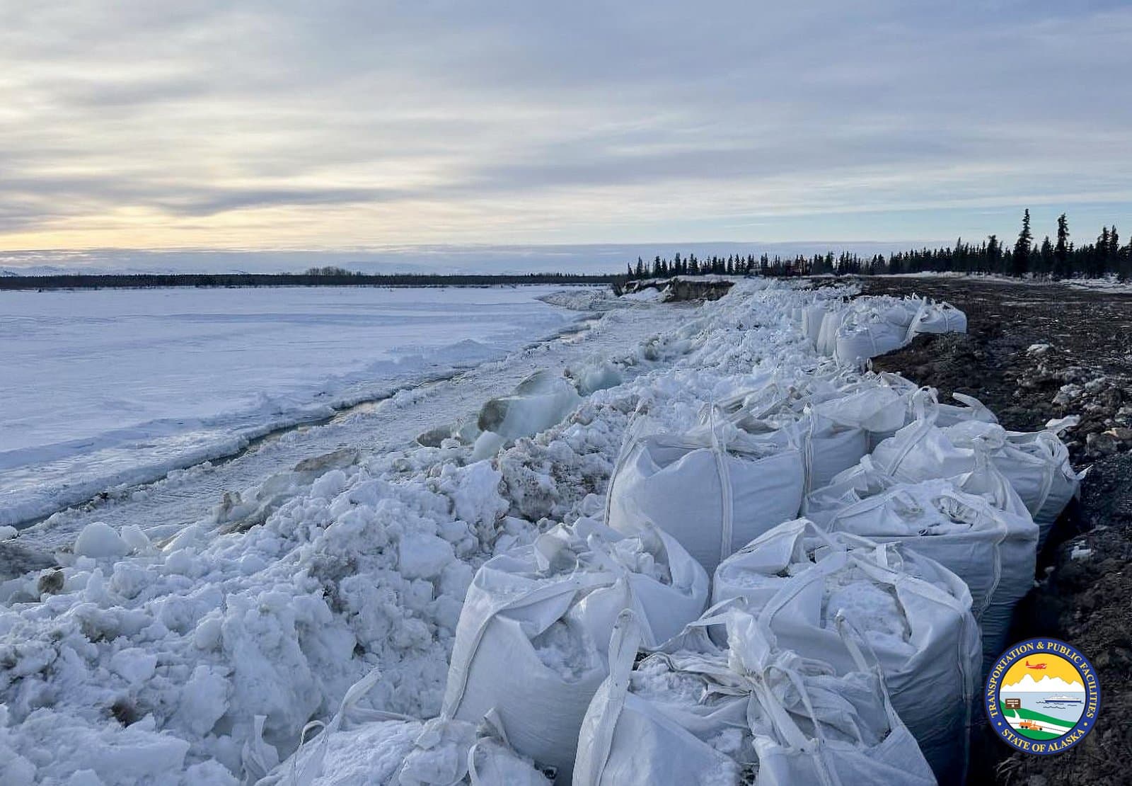Large white sandbags line the icy, snow-covered bank of the Noatak River in Alaska during the spring thaw.