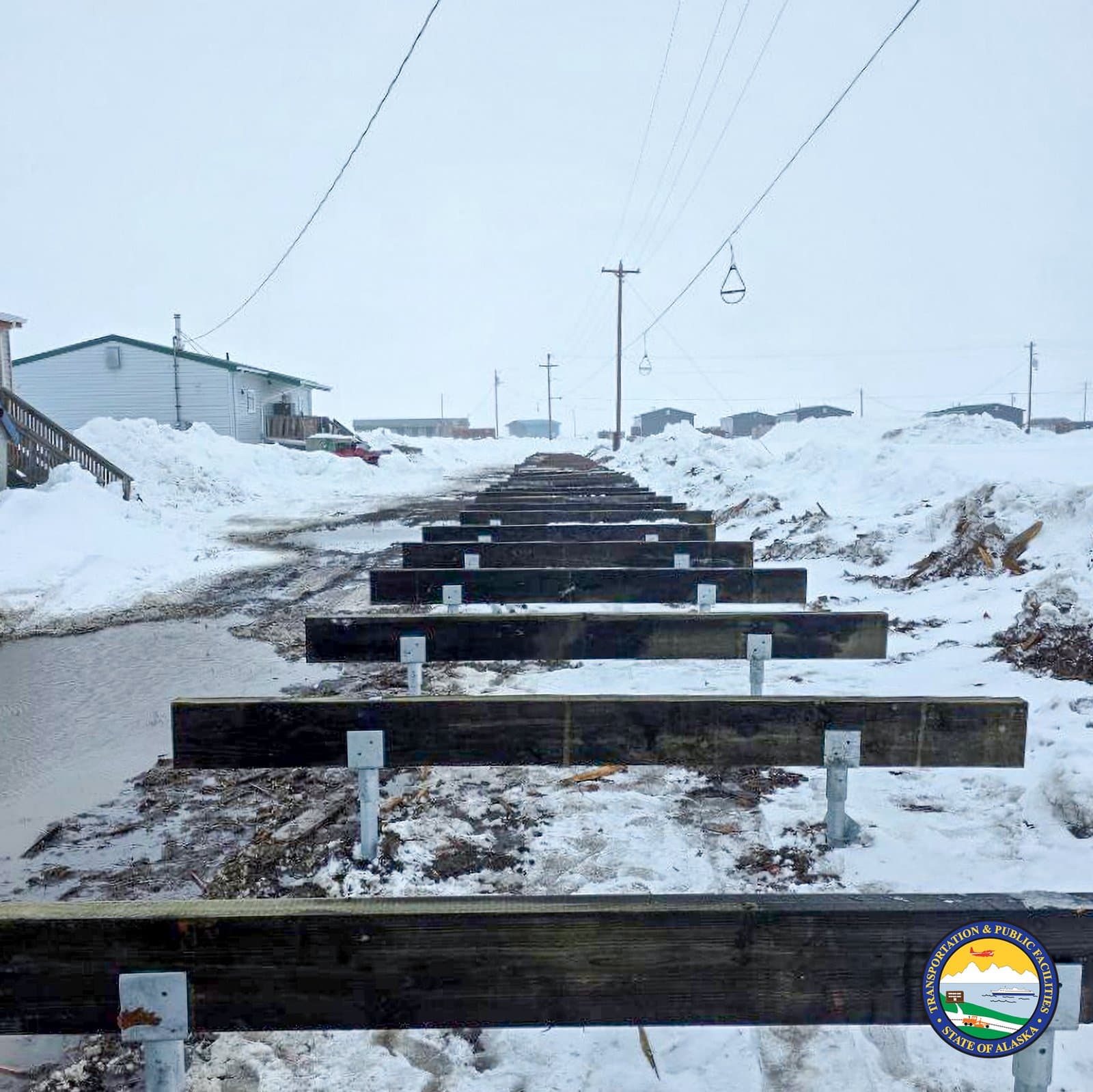 A series of wooden boardwalk supports under construction stretches across a snow-covered landscape in the rural community of Kwigillingok, Alaska.