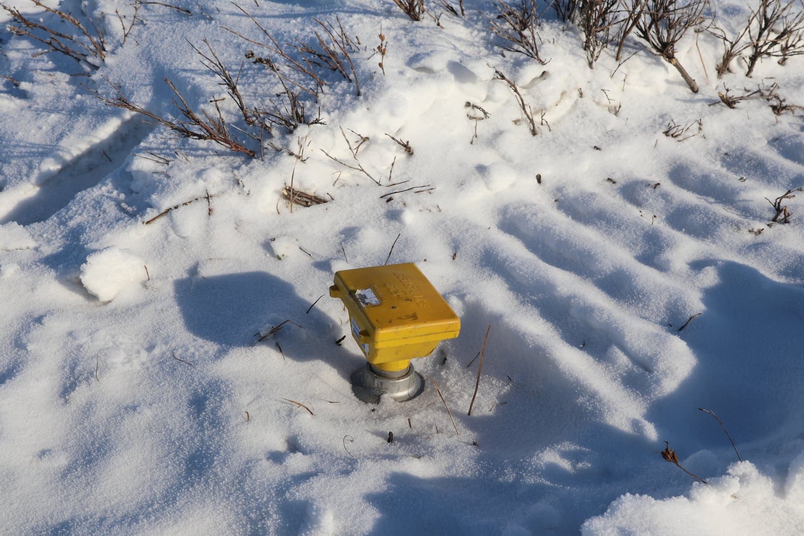 A yellow seismic node sits partially buried in a snow-covered landscape, marking a location for geophysical data collection in the field.