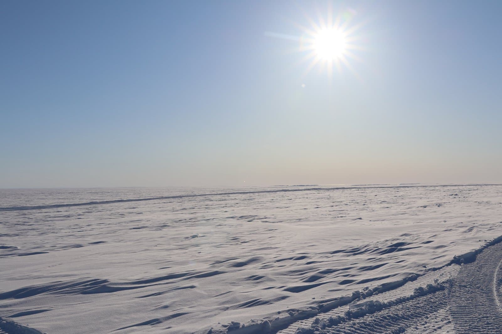 The sun hangs low over the vast, snow-covered tundra of the National Petroleum Reserve in Alaska during a clear March evening.