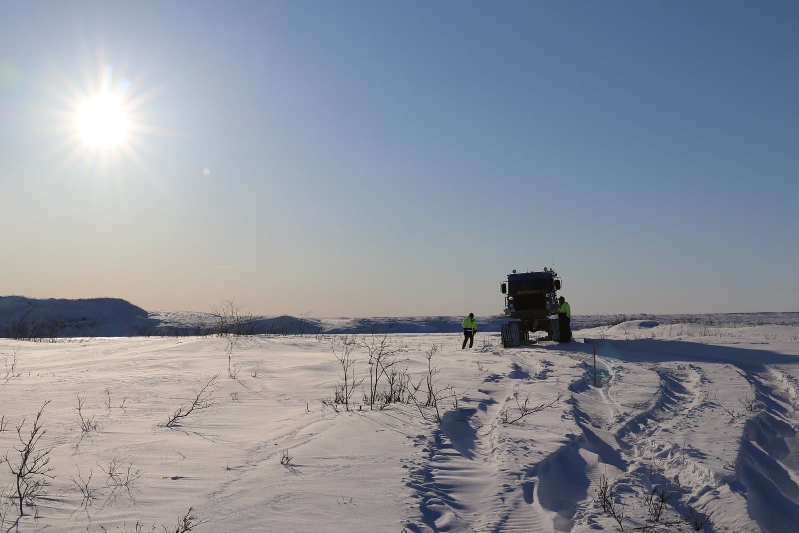 Two workers stand near a Tucker snow vehicle on a vast, snow-covered landscape within the National Petroleum Reserve in Alaska.
