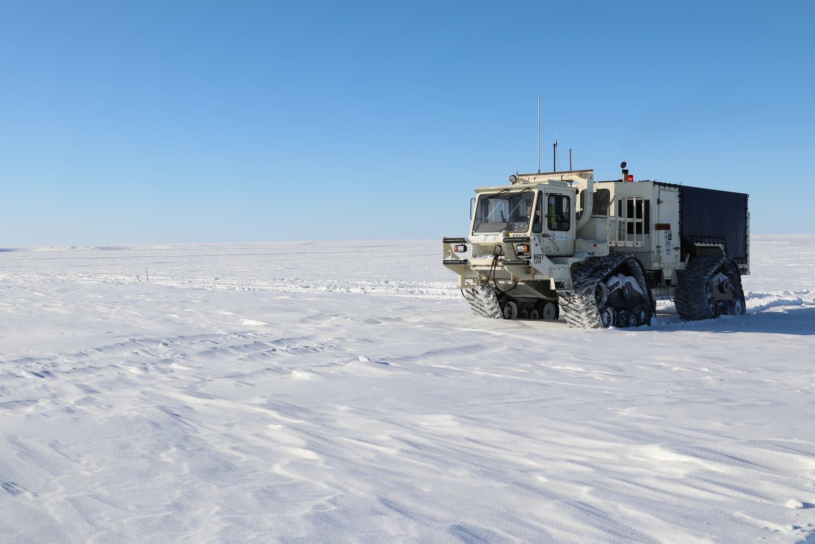 A specialized tracked vehicle traverses a vast, snow-covered landscape while collecting seismic data in a remote, treeless environment.